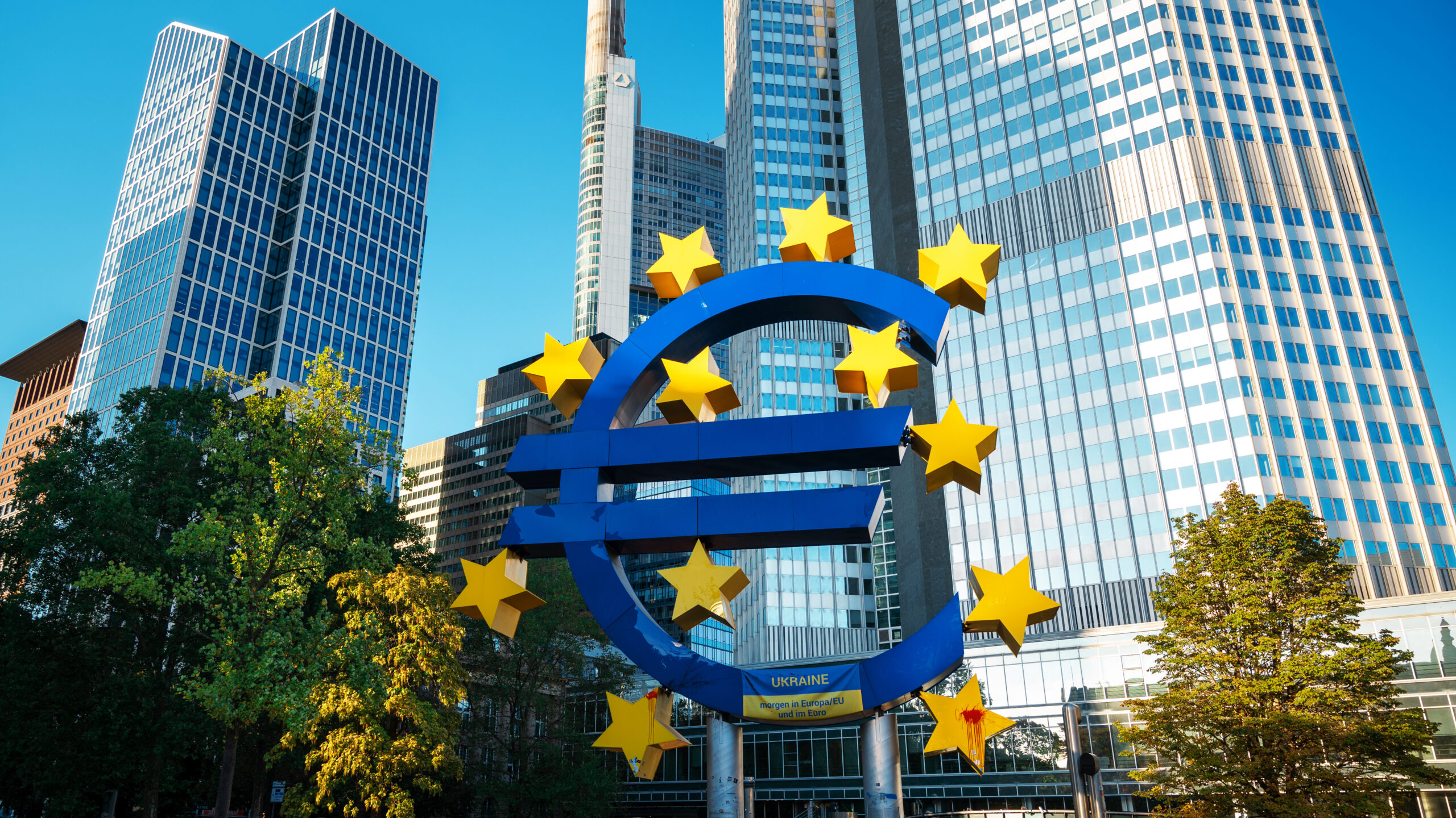 Close view of The Euro-Skulptur with multiple skyscrapers on the background in Frankfurt downtown, Germany. Flag of Ukraine and blood on it